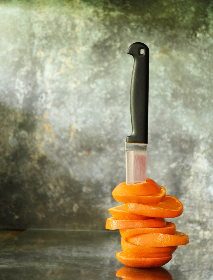 Die Orange wird mit einem alten Messer geschnitten und gestochen. auf alten Glasschreibtisch in der Küche