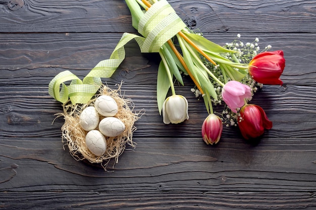 Die Osterkomposition Eier einen Strauß Tulpen und Kirchenkerzen auf Holztisch in der Nähe