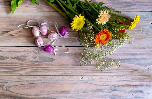 Die Osterkomposition Eier und ein Strauß bunter Gerberas auf Holztisch in der Nähe