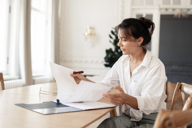 Die Person ist eine Frau, die mit Dokumenten im Büro arbeitet und eine Laptop-Arbeitsbereichsroutine verwendet