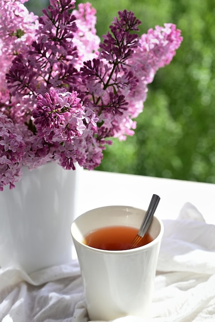 Die Postkarte ist schön Eine Tasse Tee ein altes Buch und ein Strauß lila Flieder Ein schönes Stillleben Frühlingszeit Das Konzept des Guten Morgens