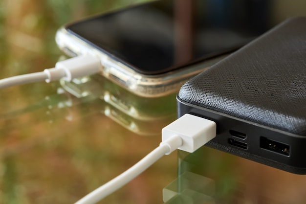 Die Powerbank lädt das Smartphone über ein USB-Kabel auf einer Glasoberfläche auf. Nahaufnahme, selektiver Fokus