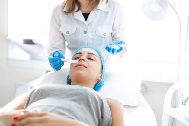 Die professionelle Kosmetikerin der Frau trägt zur Hautpflege eine Maske auf das Gesicht des Patienten auf