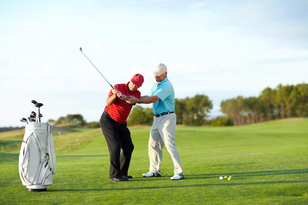 Die richtige Technik Ein männlicher Golfer bekommt Hilfe von seinem Caddy auf dem Golfplatz