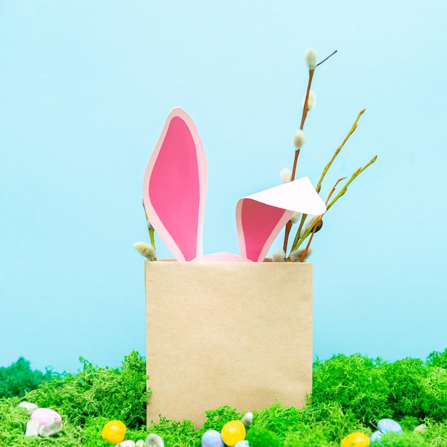 Die rosa Hasenohren ragen aus der Tasche Frühlingsgrußkarte mit Gras und Blumen auf blauem Hintergrund Ostersymbole