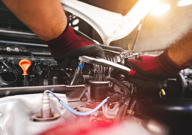 Die rote behandschuhte Hand des Automechanikers befestigt die Schraube mit dem Steckschlüssel, um den Fahrzeugmotor zu reparieren