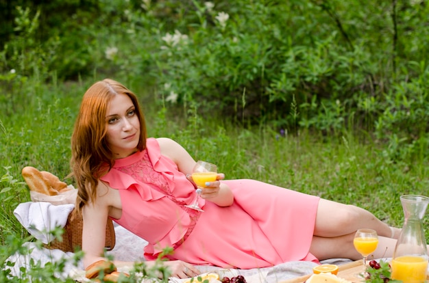 Die rothaarige Frau im rosa Kleid mit Glas Orangensaft.