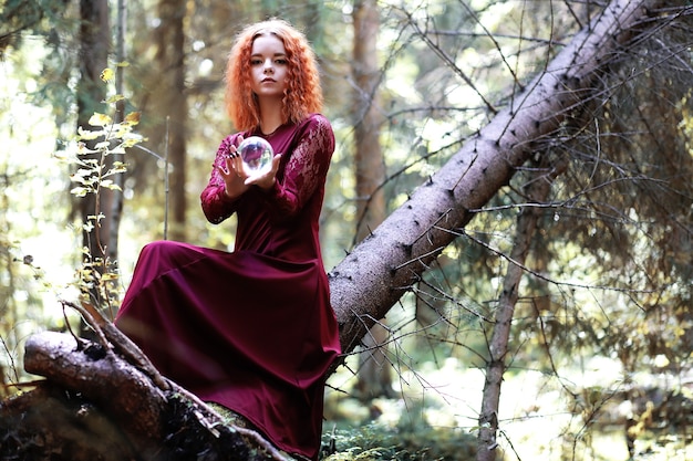 Die rothaarige Hexe hält ein Ritual mit einer Kristallkugel im Wald