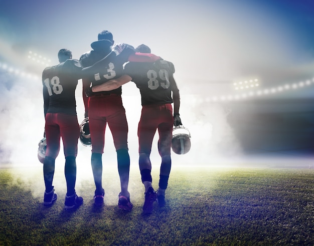 Die Rückansicht von drei kaukasischen Fitnessmännern als American-Football-Spieler auf Stadionhintergrund