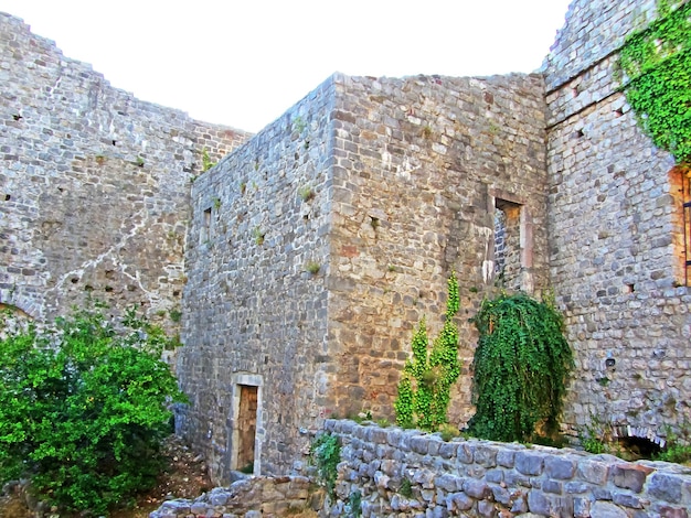 Die Ruinen einer alten Festung Alte dicke Steinmauern einer europäischen Festung, die mit Grün in den Bergen bewachsen sind Türen und Bögen in den Ruinen der Befestigungsanlagen