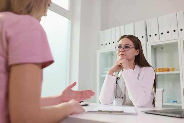 Die Ärztin hört ihrer Patientin zu, während sie in der medizinischen Klinik am Tisch sitzt