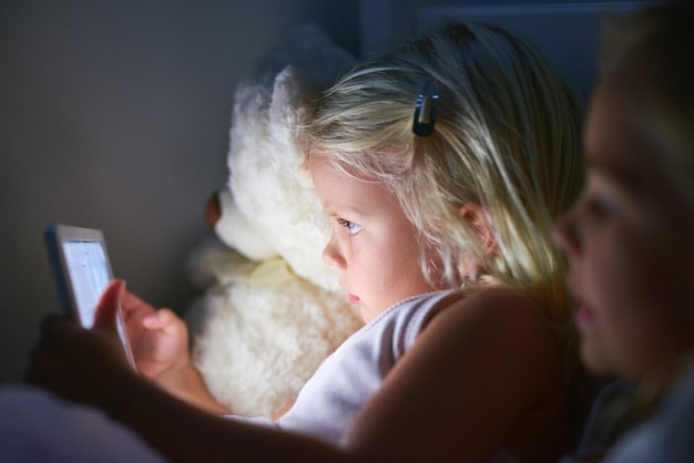 Die Schlafenszeit ist viel interaktiver geworden Aufnahme von zwei kleinen Mädchen, die vor dem Schlafengehen ein digitales Tablet verwenden