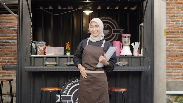 Die schöne asiatische Kellnerin bringt eine Liste mit gebrauchsfertigen Menüs am Café-Standcontainer