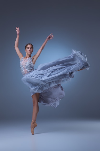 Die schöne Ballerina tanzt im langen blauen Kleid auf blauem Hintergrund