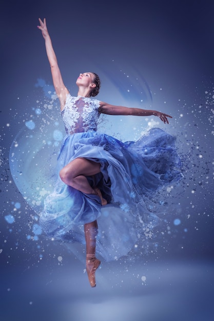 Die schöne Ballerina tanzt im langen blauen Kleid auf blauem Untergrund