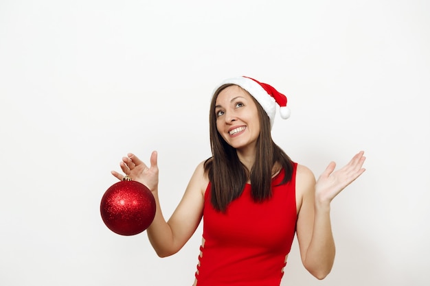 Die schöne europäische brünette junge glückliche frau mit charmantem lächeln im roten kleid und weihnachtshut, die großes glänzendes baumspielzeug auf weißem hintergrund hält. Sankt-Mädchen isoliert. Neujahrsferien 2018 Konzept