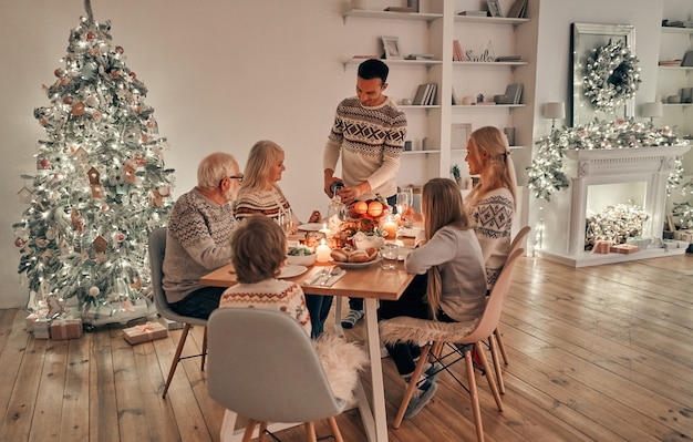 Die schöne Familie, die auf dem Weihnachtsbaumhintergrund zu Abend isst