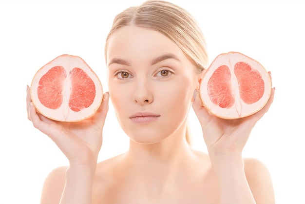 Die schöne Frau, die eine Grapefruit auf dem weißen Hintergrund hält