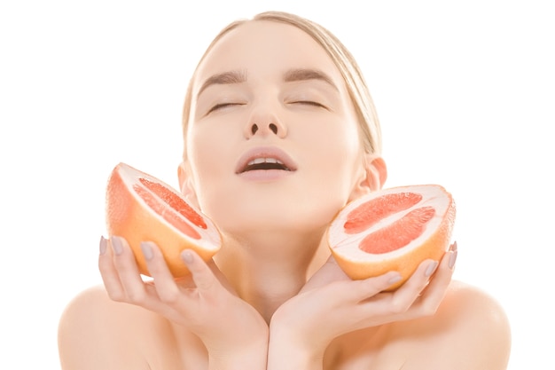 Die schöne Frau, die eine Grapefruit auf dem weißen Hintergrund hält