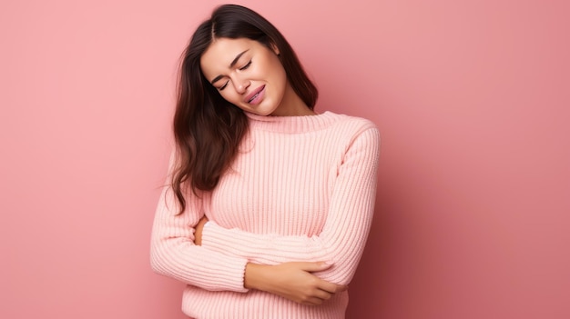 Die schöne junge brünette Frau im Pullover leidet unter Bauchschmerzen, isoliert auf rosa Hintergrund