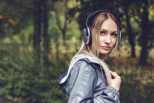 Die schöne junge Frau, die auf den Stadtpark geht, genießt, Musik auf Kopfhörern zu hören.