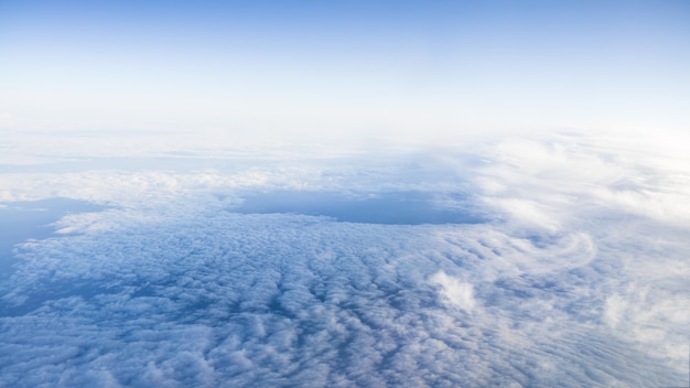 Die schöne Wolkenlandschaft mit klarem blauem Himmel. Panorama über weißen Wolken, wie durch das Fenster eines Flugzeugs gesehen. Ein Blick aus dem Flugzeugfenster