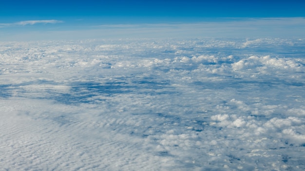 Die schöne Wolkenlandschaft mit klarem blauem Himmel. Panorama über weißen Wolken, wie durch das Fenster eines Flugzeugs gesehen. Ein Blick aus dem Flugzeugfenster