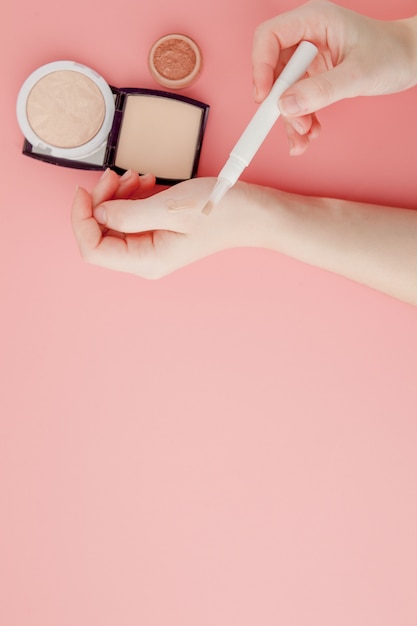Die Schönheitsbloggerhände der Frau halten professionelle Hi-End-Kosmetik des Flaschen- und Röhren-Spa auf rosa Hintergrund, Minimalismuskonzept, warmen gemütlichen Tönen und Copyspace