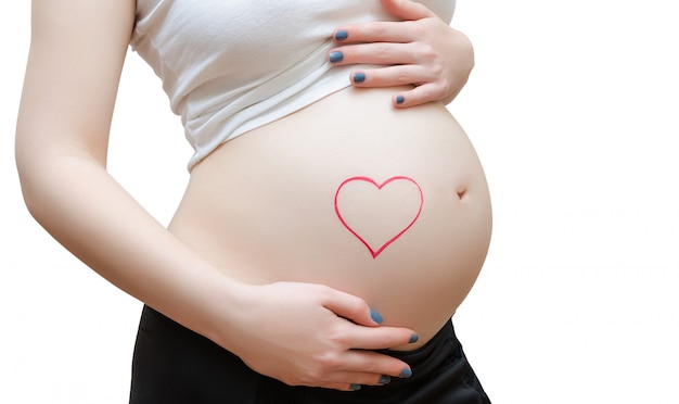 Die schwangere Frau auf weißer Wand Gemaltes Herz auf dem Bauch.