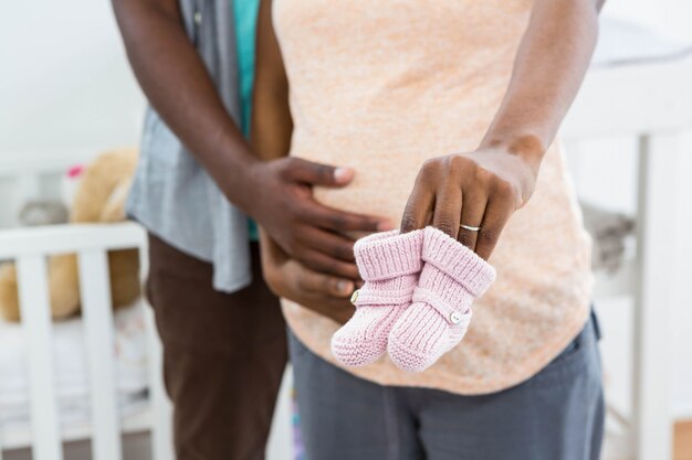 Die schwangeren Paare, die rosa Babyschuhe halten, nähern sich Wiege