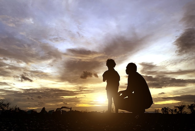 Die Silhouette des Vaters und des Sohnes, die den Sonnenuntergang für Vatertagsliebesfeiertagskonzept genossen