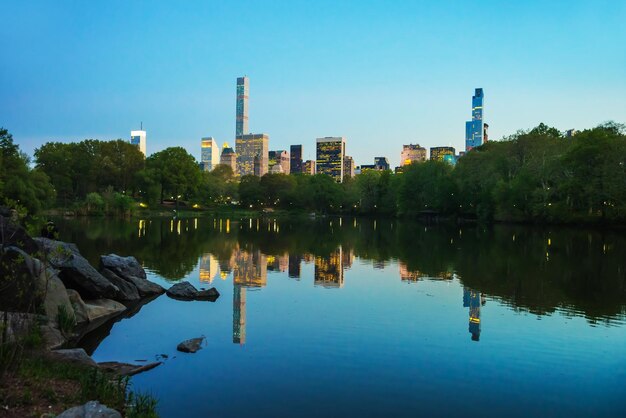 Die Skyline von Midtown Manhattan spiegelt sich im Central Park im Wasser wider. New York, New York, USA. Abends beleuchtete Wolkenkratzer.