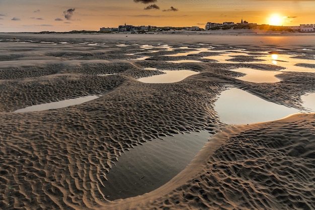 Die Sonne geht hinter der Kirche auf und die Gebäude der Küste hinter den Pfützen des Strandes