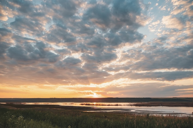 Die Sonne geht über dem Hügel auf und beleuchtet einen See im Tal. Schöne Märchenlandschaft. Glänzender Sonnenaufgang, der Sonnenstrahlen in einem See mit Pelikanen reflektiert