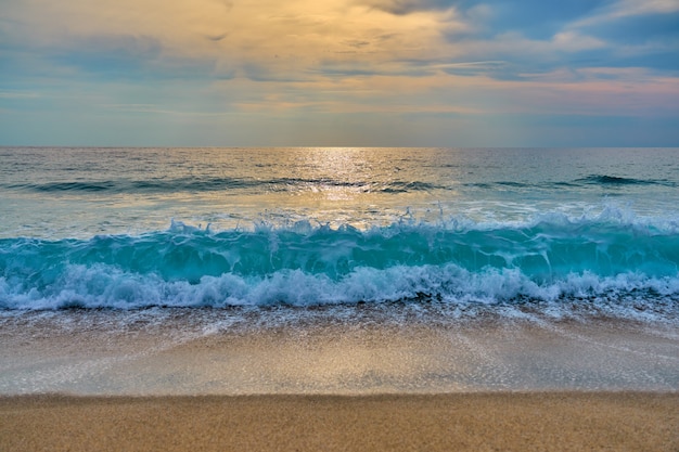 Foto die sonne hinter den wolken reflektiert wasser und wellen mit schaum, der auf sand trifft.