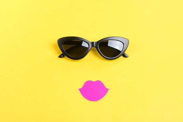 Die Sonne mit stilvoller schwarzer Sonnenbrille, rosa Lippen auf gelber Liegefläche