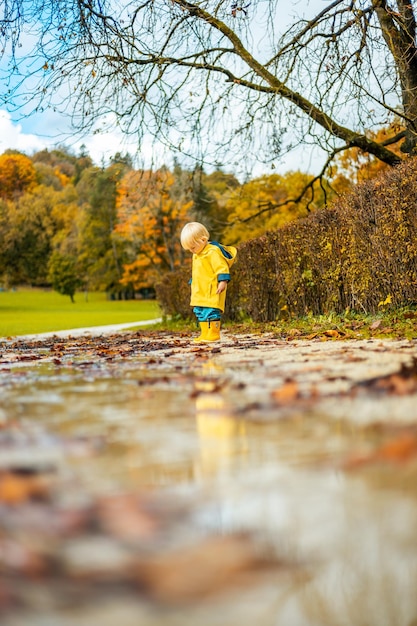 Die Sonne scheint immer nach dem Regen kleine Bindung Säugling Junge trägt gelbe Gummistiefel und gelb