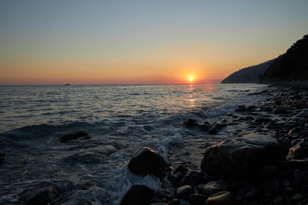 Foto die sonne taucht unter dem horizont, die felsige küstenlinie, die natur, die schönheit in der ruhigen ruhe, die wellen schlagen sanft gegen das ufer, während die silhouetten der klippen majestätisch gegen den dunklen himmel stehen.