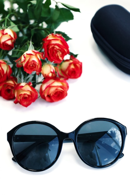 Die Sonnenbrille der Frauen auf weißem Hintergrund mit Rosen und Fall. Optik speichern, schützen Sie Ihre Augen vor UV-Licht.