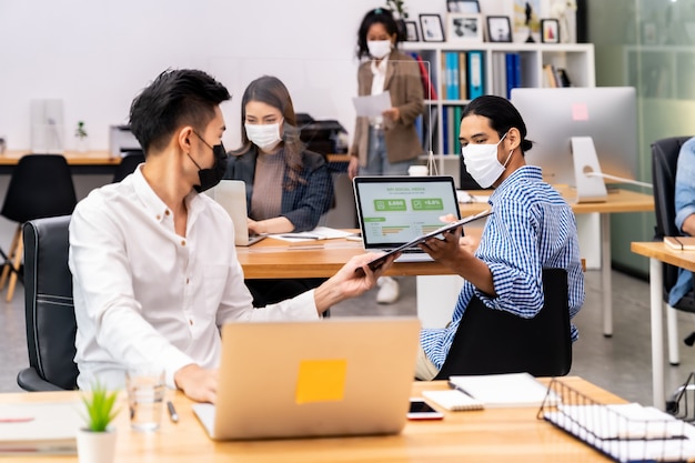 Die soziale Distanz im Büro mit dem Business-Team, das Gesichtsmasken trägt