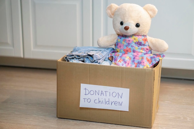 Foto die spendenbox für kinderkleidung steht nicht auf dem boden. spielzeug und babysachen im karton. spenden- und charity-konzept