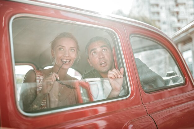 Die Stadt bewundern. Erstaunte Touristen, die aus den Fenstern des roten Retro-Autos schauen, Frau lächelt und beißt in ihre Brille und Mann öffnet den Mund.