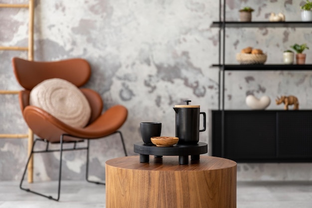 Die stilvolle Komposition des Wabi-Sabi-Interieurs mit Couchtisch, schwarzen Accessoires, Sessel und Regal Graue Betonwand Wohnkultur Vorlage