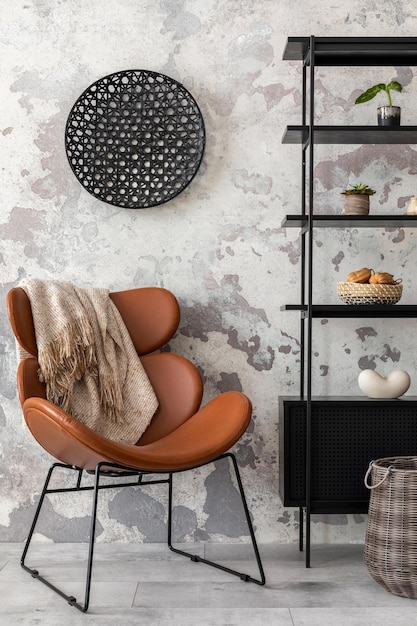 Die stilvolle komposition des wabi-sabi-interieurs mit schwarzem gestell, braunem sessel mit plaid und persönlichem zubehör. graue betonwand wohnkultur-vorlage