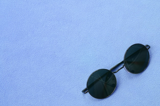 Die stilvolle schwarze Sonnenbrille mit runder Brille liegt auf einer Decke aus weichem, hellblauem Fleece.