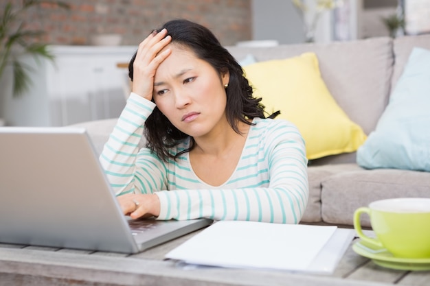 Die Stirn runzelnder Brunette, der Laptop im Wohnzimmer verwendet