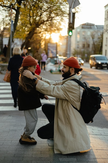 Die Straße überqueren auf einer Fußgängerüberquerung Ein Spaziergang einer kleinen Tochter zusammen mit einem jungen Vater in der Mitte der Abendstraßen einer belebten Stadt