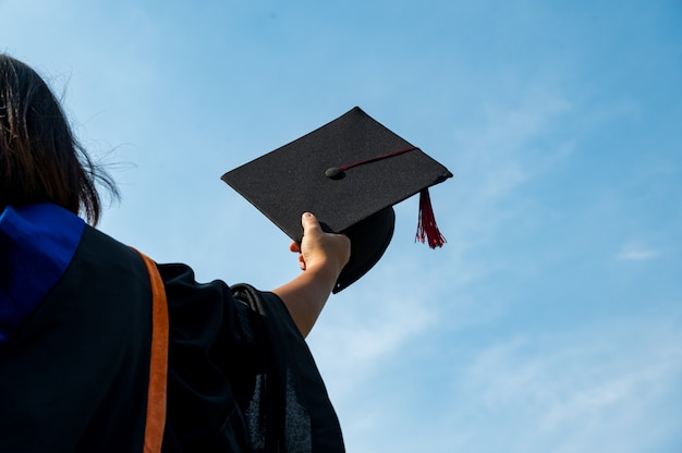 Die Studenten halten einen Schuss Abschlusskappe an der Hand in einem hellen Himmel