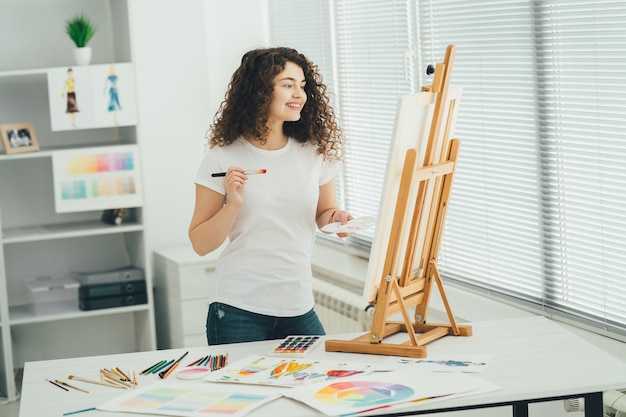 Die süße Frau mit einem Kunstpinsel malt ein Bild auf der Staffelei