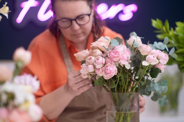 Foto die talentierte floristin arbeitet mit zarten rosafarbenen rosen und pfingstrosen und fertigt atemberaubende arrangements